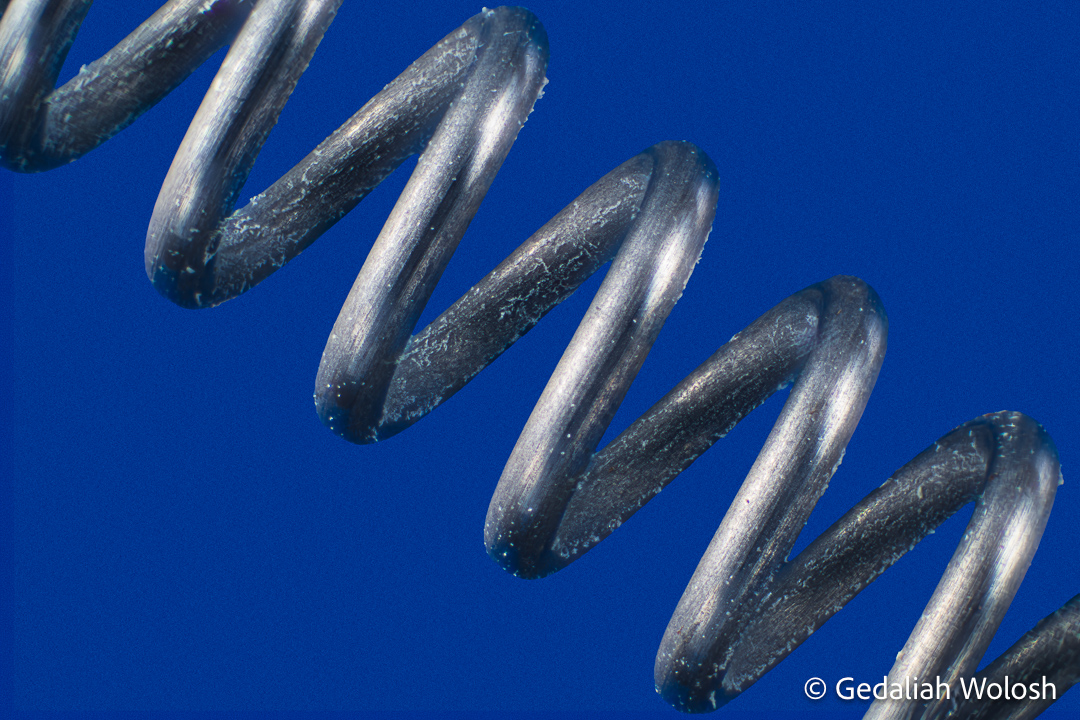 Industrial Rhythm A compression spring photographed at approximately 3.5× magnification reveals a repeating sequence of polished curves...